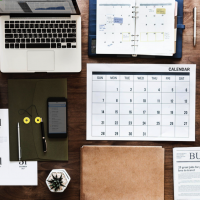 An organized desk with computer, planner, calendar, and more